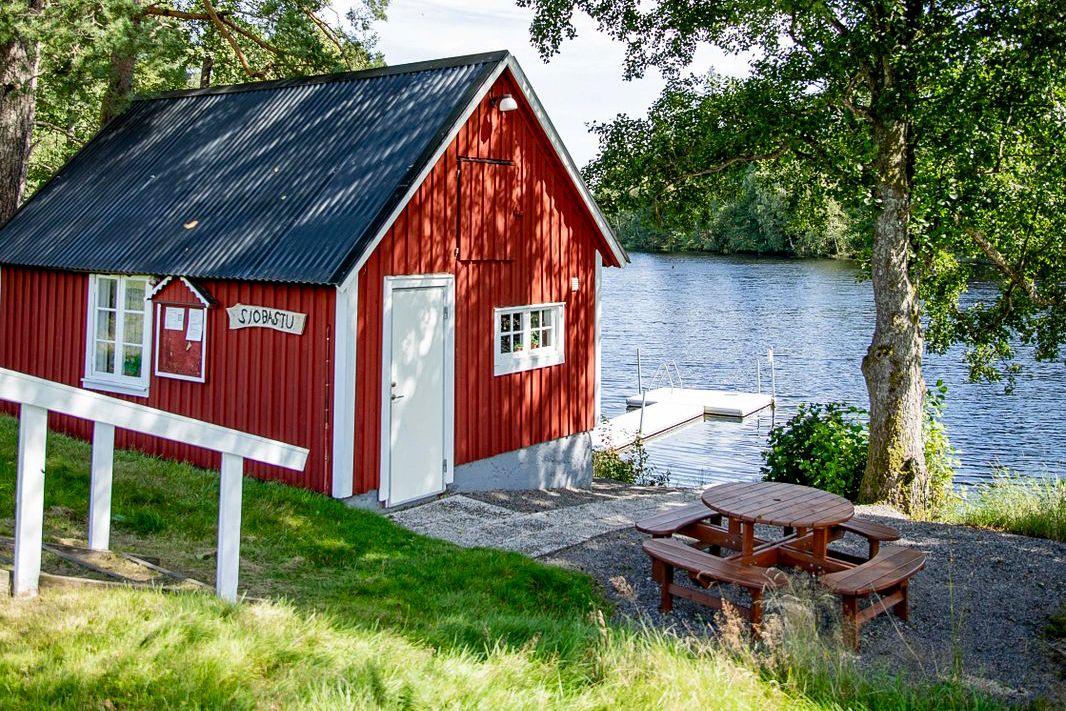 En röd bastustuga med ett picknickbord och utsikt över Eseredssjön.
